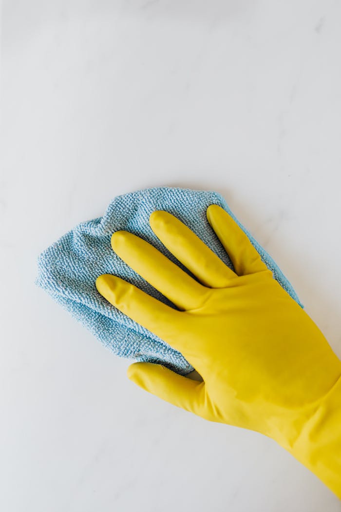 Top view of crop anonymous housekeeper in protective gloves cleaning and polishing white surface with blue rag